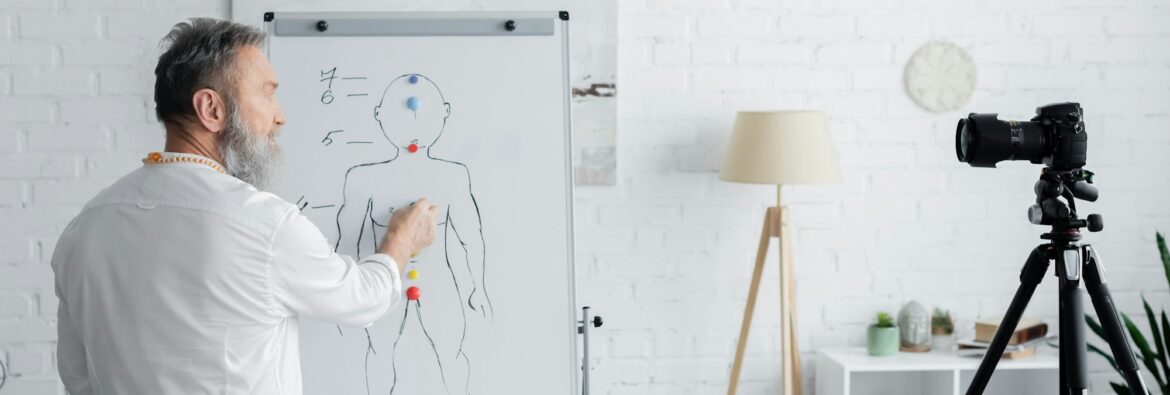 ayurveda guru near flip chart with human chakras system and digital camera