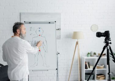 ayurveda guru near flip chart with human chakras system and digital camera